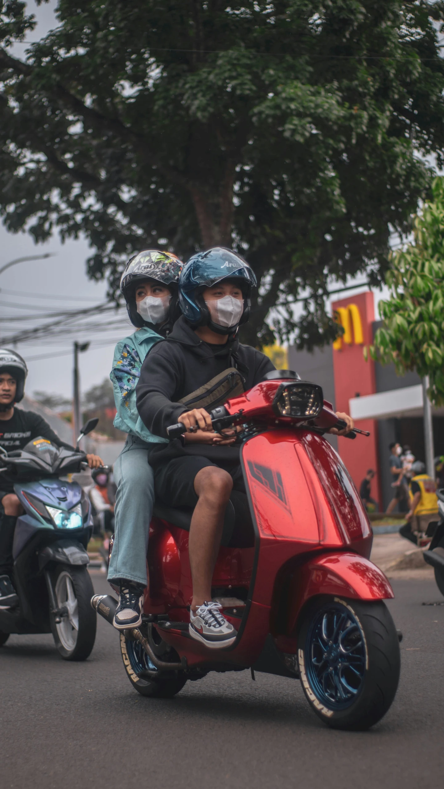 a man and woman on a red scooter riding past a green tree