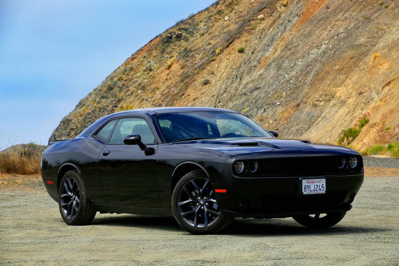 a dark car on a dirt road next to a mountain