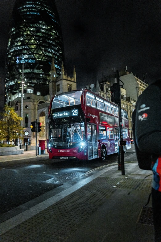 a large red bus driving past a tall building at night