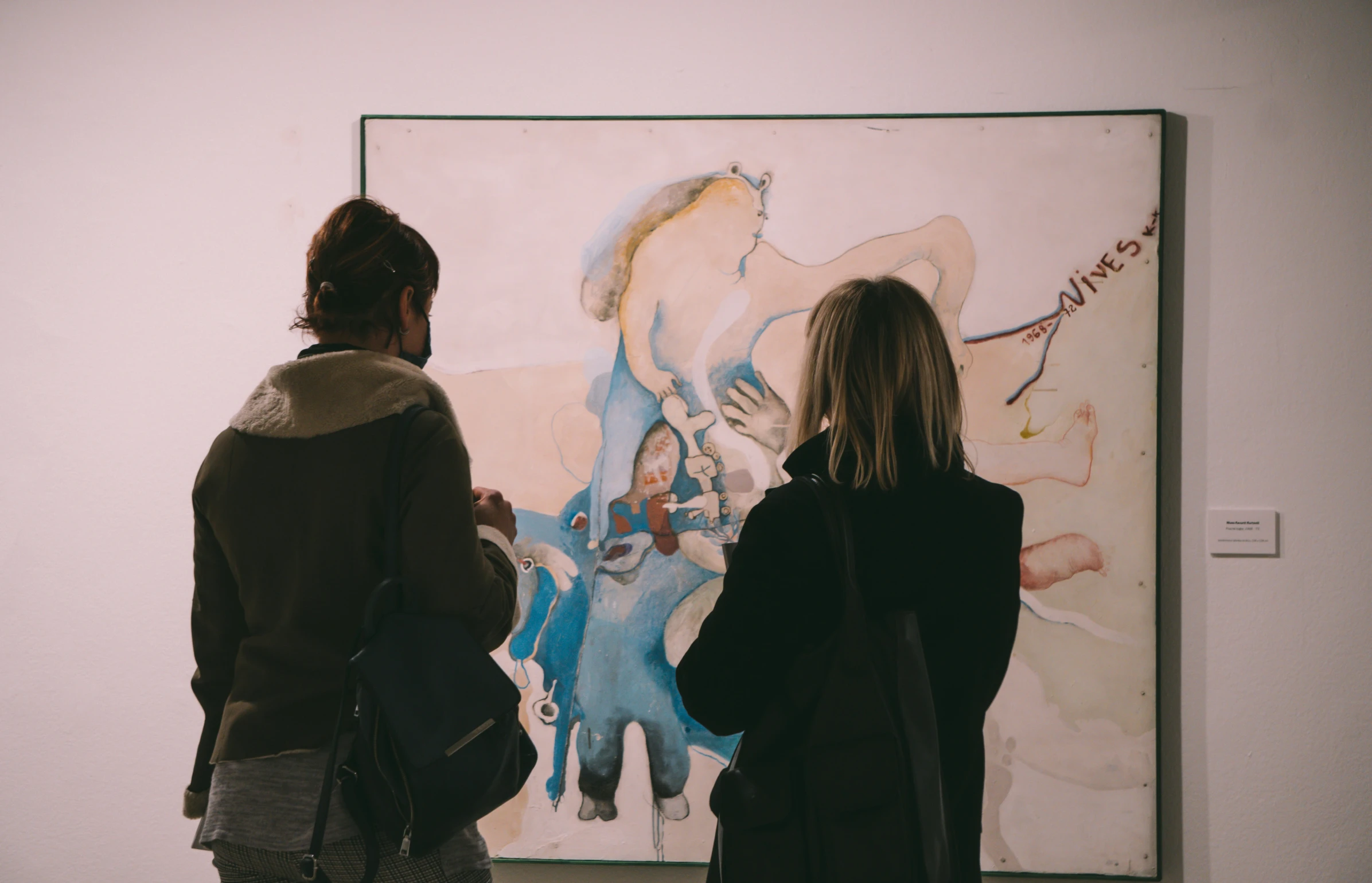 a couple of people looking at art on a wall