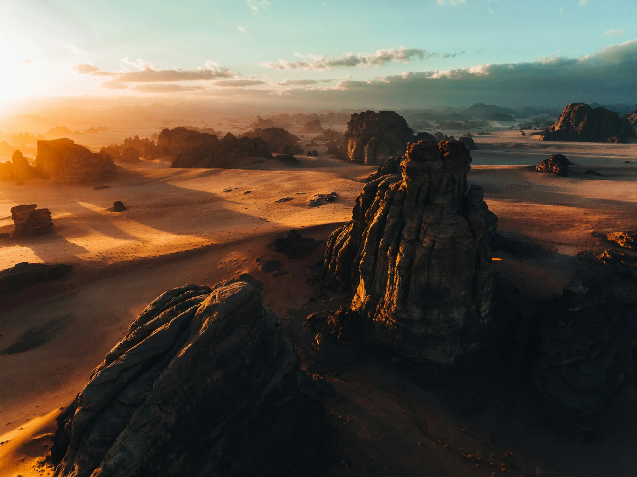 the sunsets over desert terrain with large rocks in the foreground