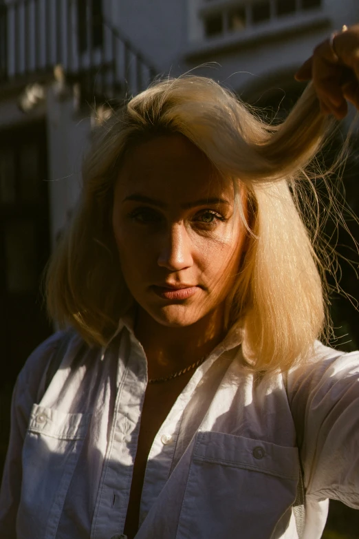 a woman with long blonde hair and white shirt holding her hair close to the camera