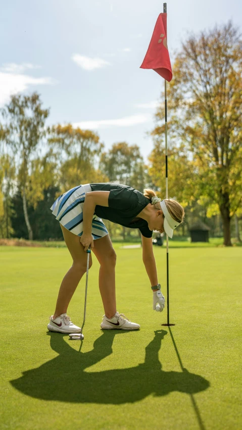 a girl in striped shorts putting a golf ball on to the green