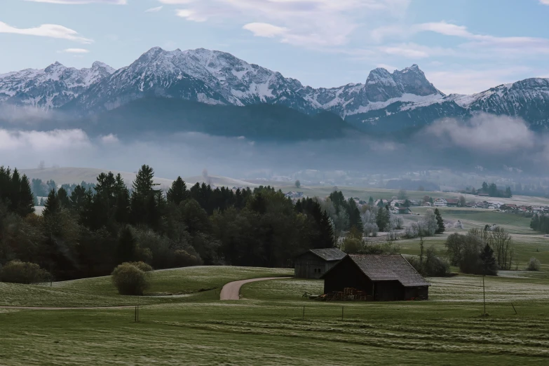 a barn sits in a grassy field surrounded by tall, snowy mountains