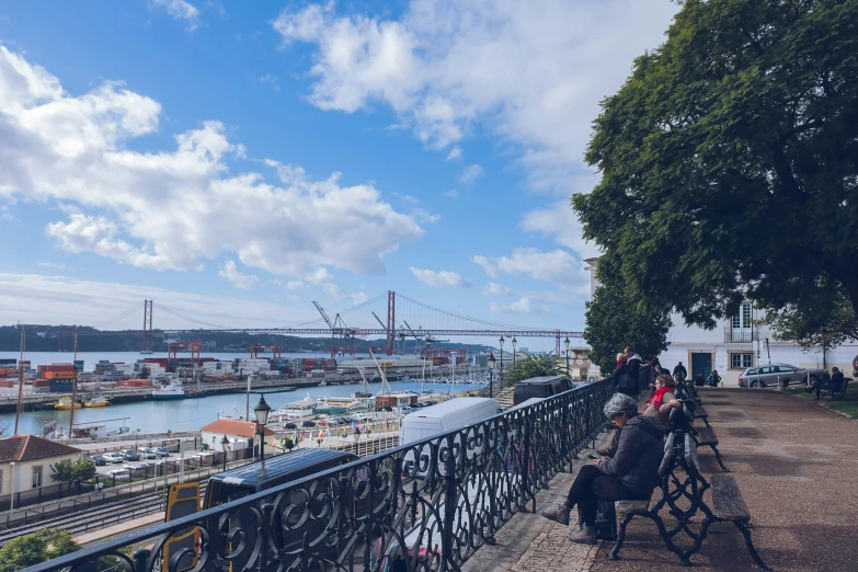 people sitting at benches on a walkway overlooking the water