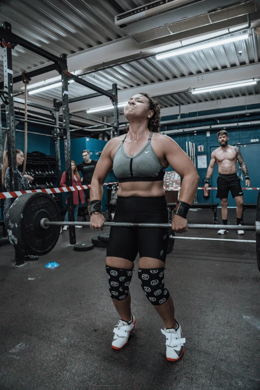 a woman in a grey tank top is holding a barbell in a gym