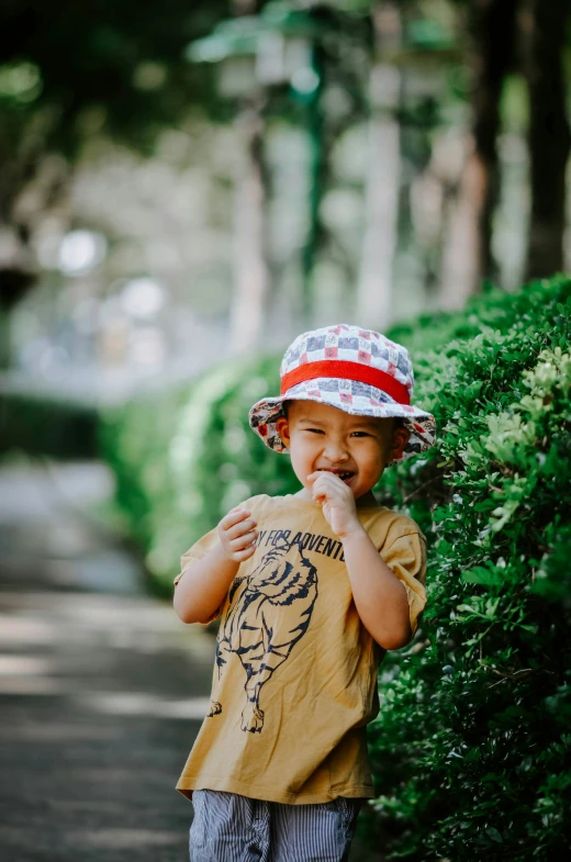 a boy wearing a red and white hat, brown shirt, and shorts is eating food on a walkway