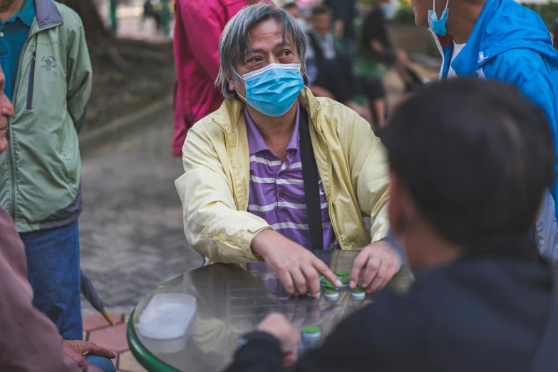 a man in a face mask and yellow jacket sits at a table