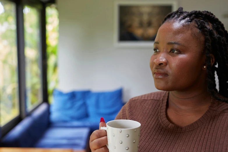 a woman with dreadlocks and red fingernails holds a white coffee mug