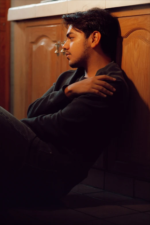 a man sitting against a wooden cabinet looking to his left