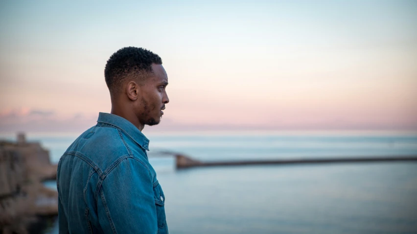 a man standing in front of the ocean looking at the sky