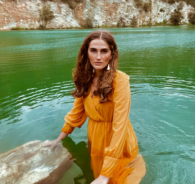 a woman in yellow dress standing in water with rock