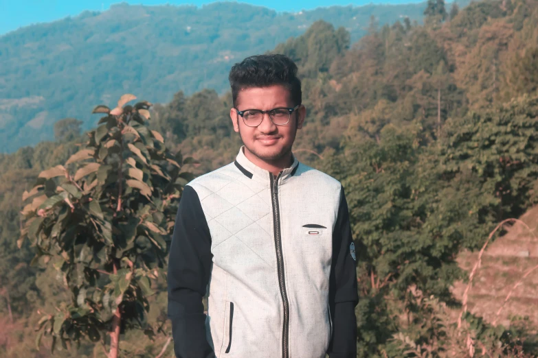 a man wearing glasses standing in front of mountains