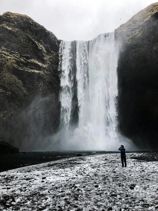 the person stands alone beneath a waterfall in a desert