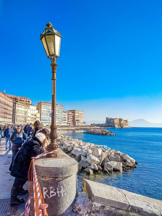 people are walking along a river by a street lamp