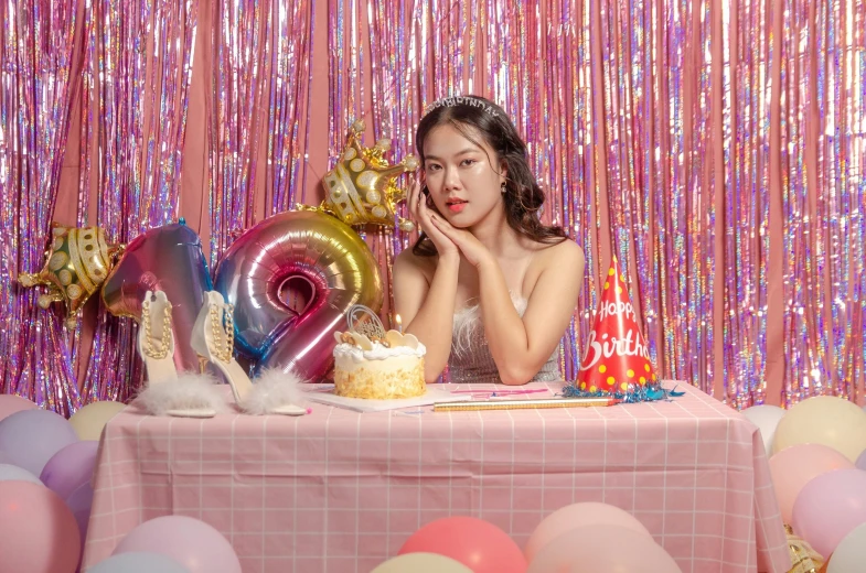 a young woman sitting at a table with balloons and birthday decorations