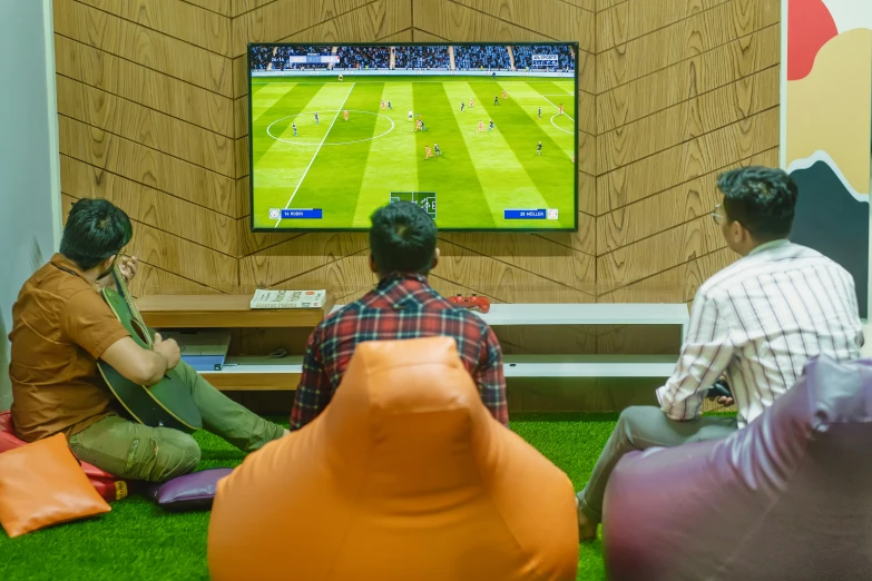 two men sit in front of the tv watching soccer