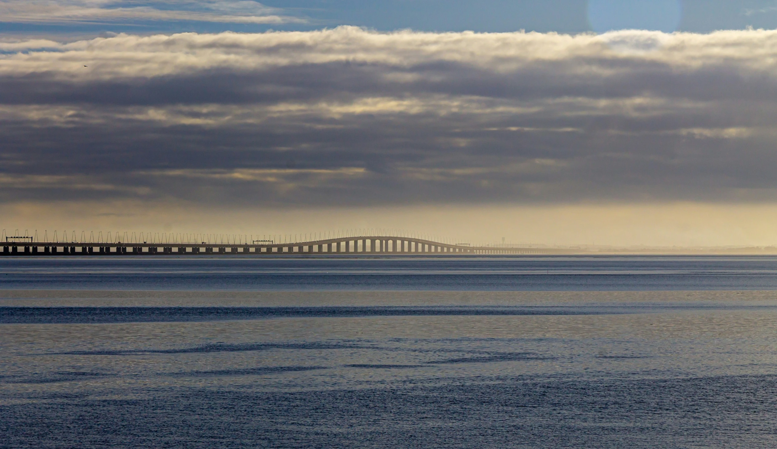 a large bridge is over the ocean with its cloudy sky