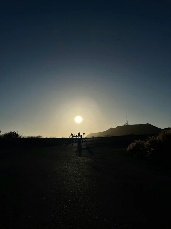 a silhouette of the sun and people riding in the background