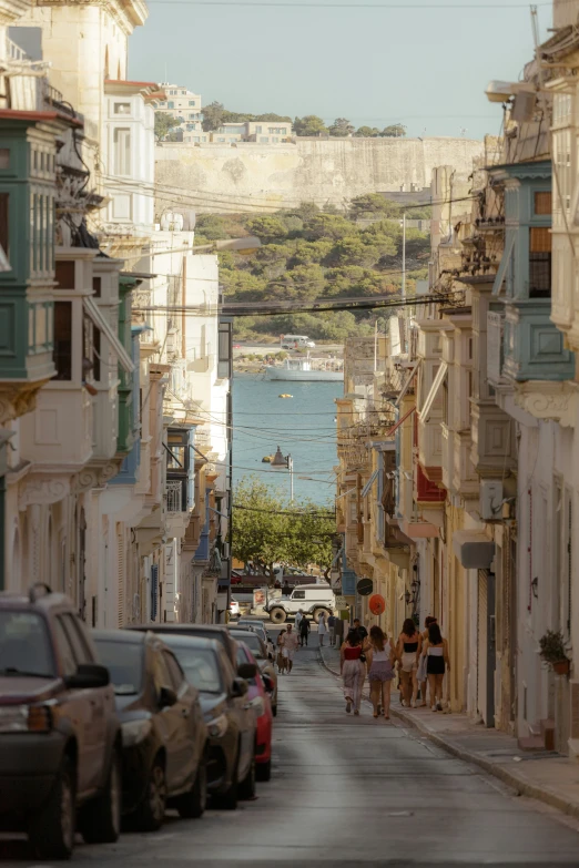 a city street with parked cars and some people walking on the sidewalk