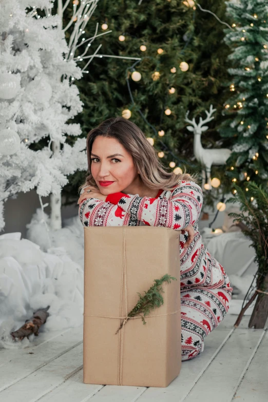 a woman is sitting next to a christmas tree and holding a brown paper bag