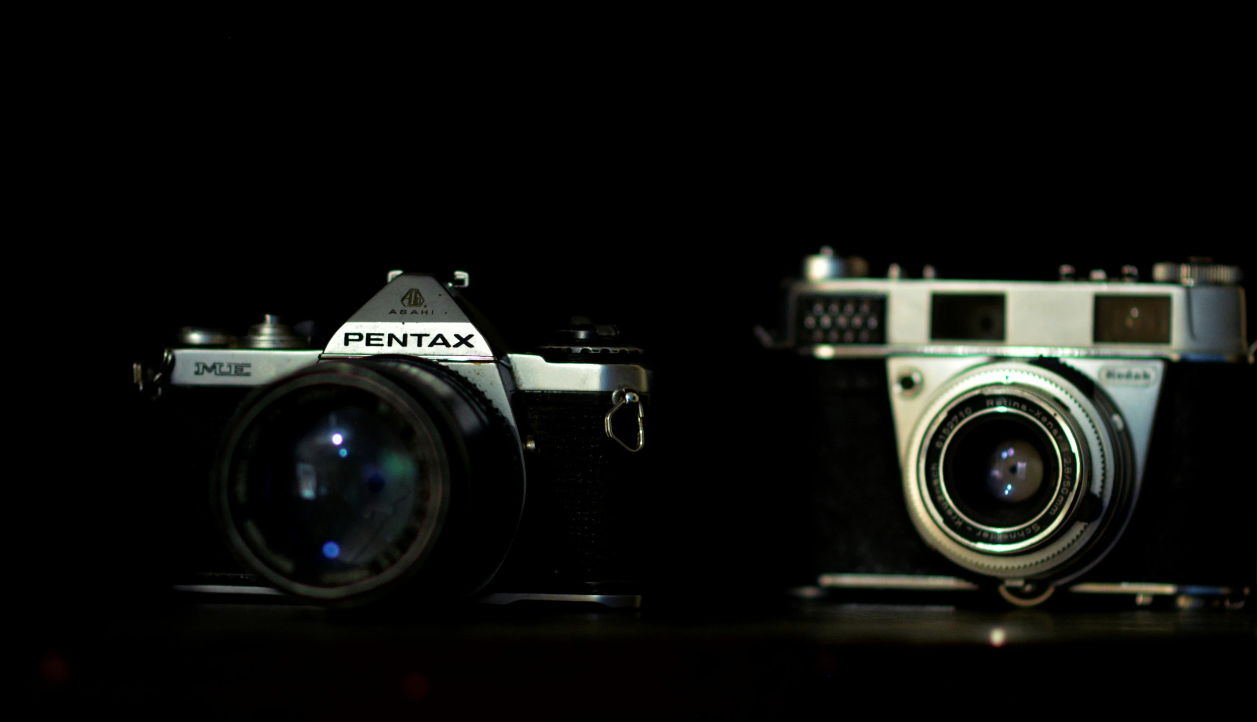 two camera's, one silver, the other brown, sit side by side