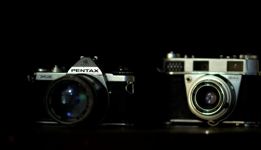 two camera's, one silver, the other brown, sit side by side