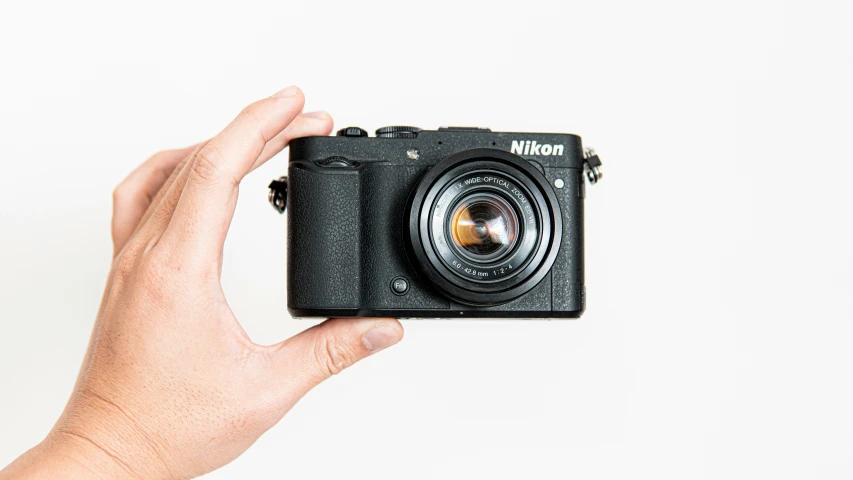 a hand holding a camera next to a white background