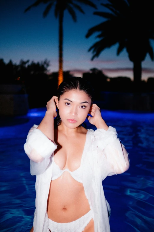 a woman in white clothes is standing near a pool at night