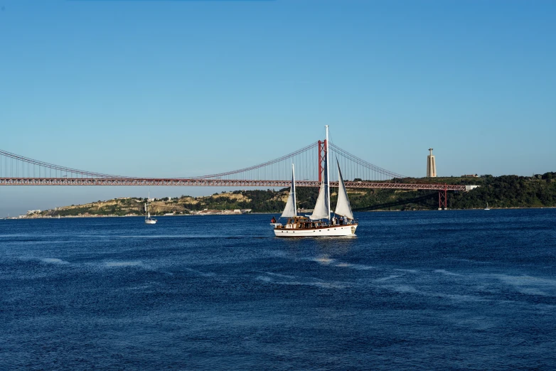 a ship sailing in a blue ocean next to a large bridge