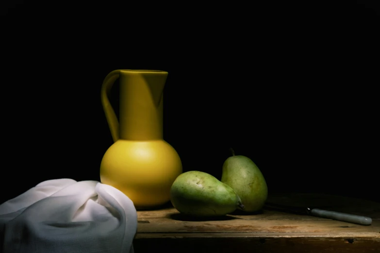 a wooden table topped with yellow vase next to pears and a white cloth