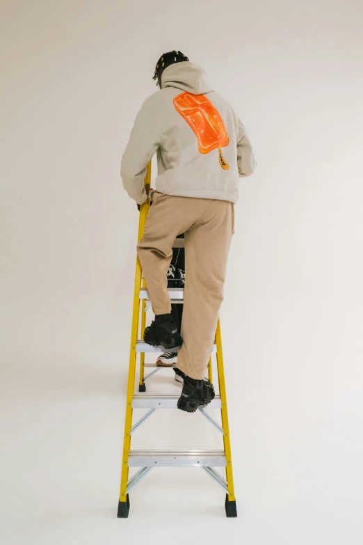 man in hoodie on a step ladder leaning against the wall