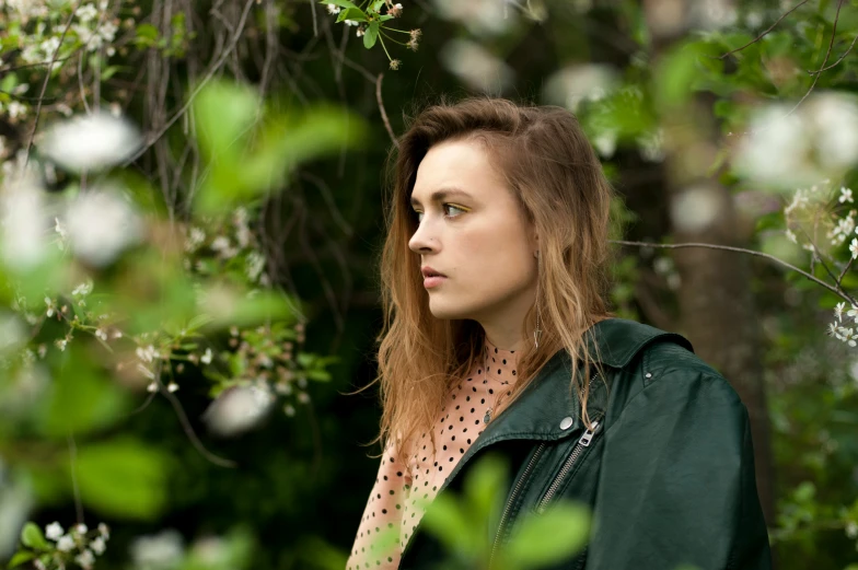 a woman standing in a forest next to green leaves