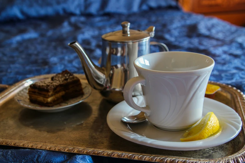 a cup on a plate with a slice of cake and a tea kettle