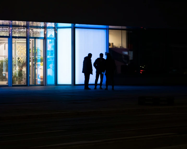 three people are standing in front of a tall building at night