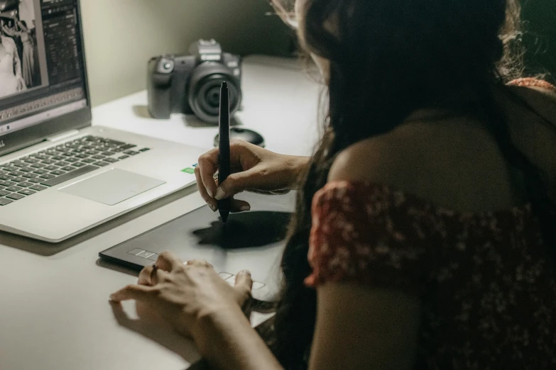 a woman sitting at her laptop with a camera on the desk in front of her