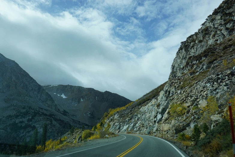 a road with steep side of mountain and some clouds in the sky