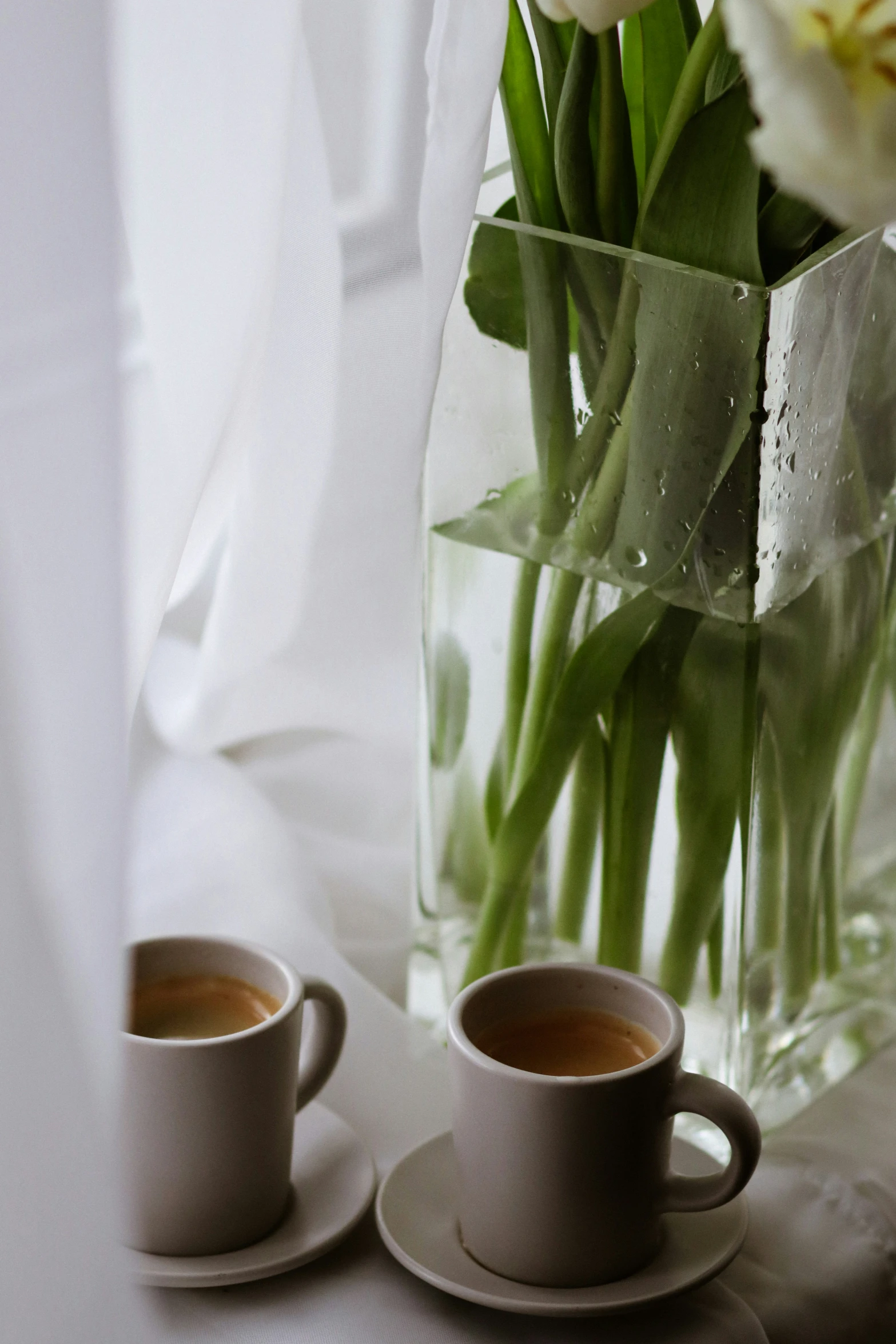 a vase with some flowers in it next to two mugs with coffee