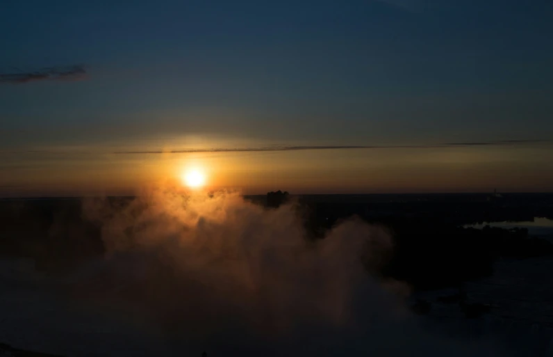 the sun rises behind steam rising from a body of water