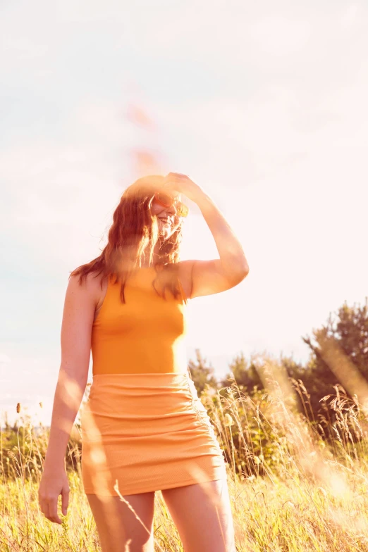 a woman standing in a field while wearing an orange dress