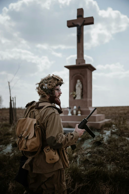 the soldier is wearing a uniform and is holding his weapon near a cross