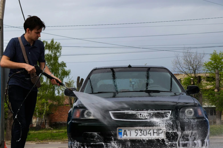 man washing black car while holding a water hose