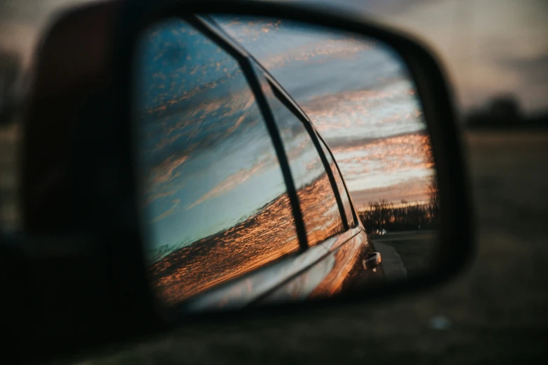 a rear view mirror reflecting the sunset and sky