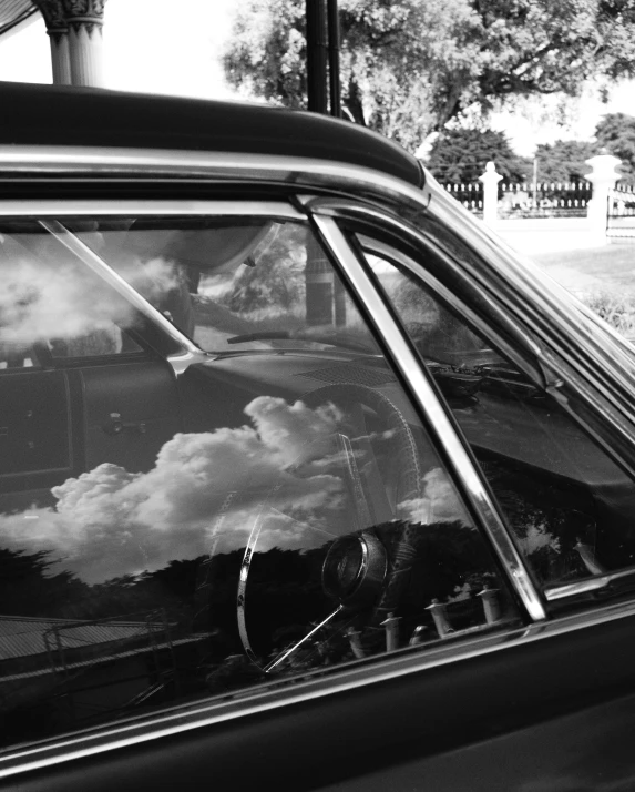 the reflection of clouds in the window of a vintage car