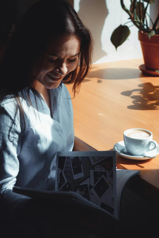 a woman holding an open magazine while sitting at a wooden table