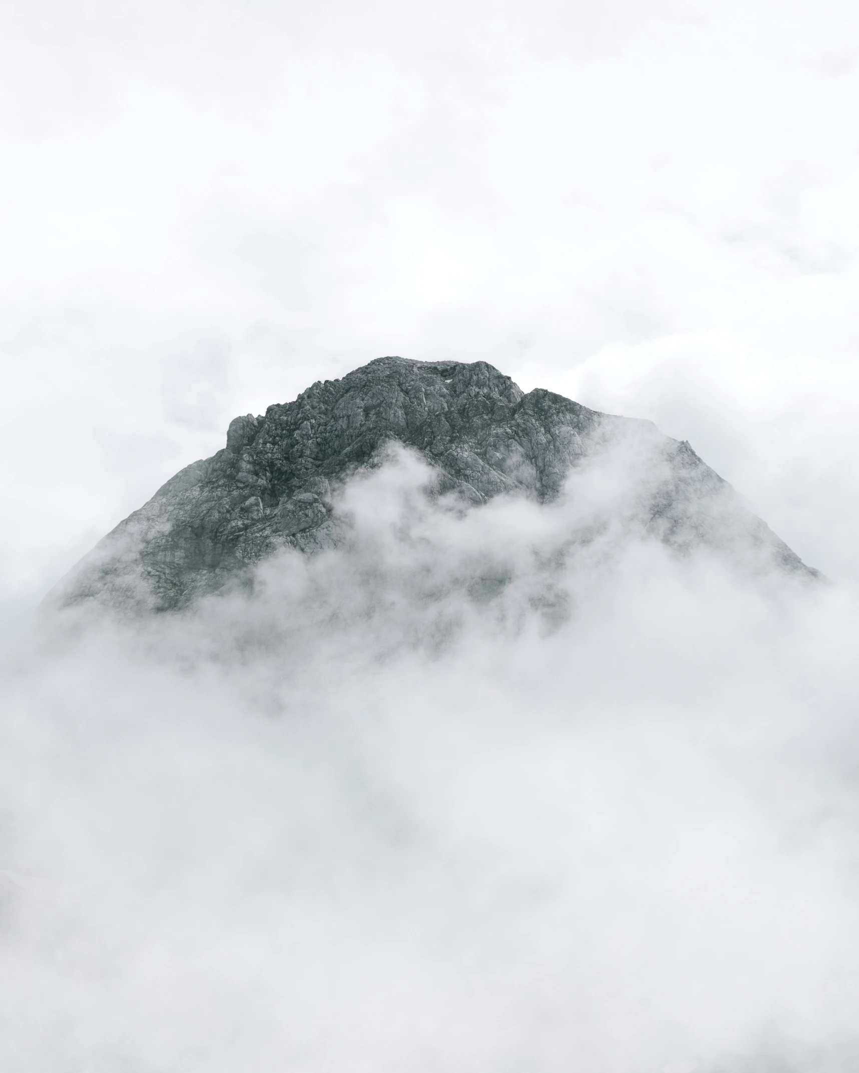 a mountain peak rises above clouds in the sky