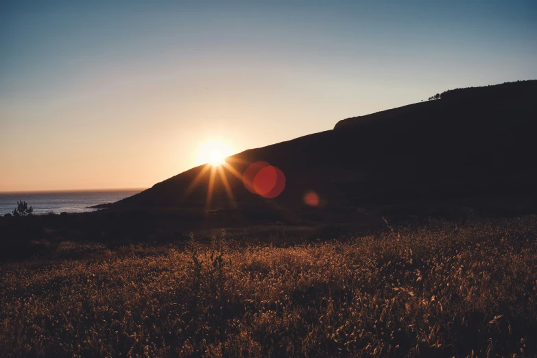 the sun setting behind a mountain, behind a field