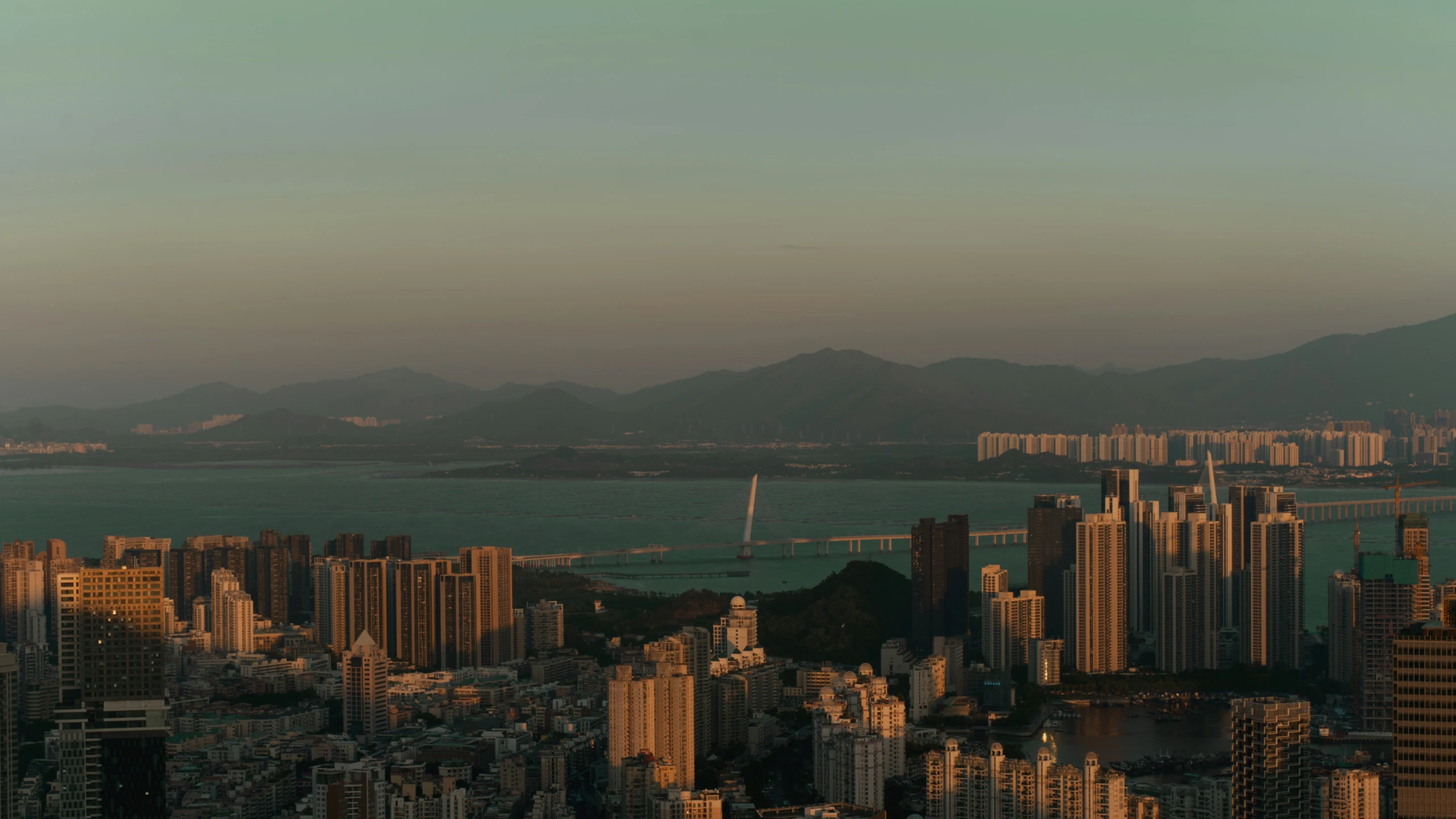 a view of a city and the ocean, with mountains in the distance