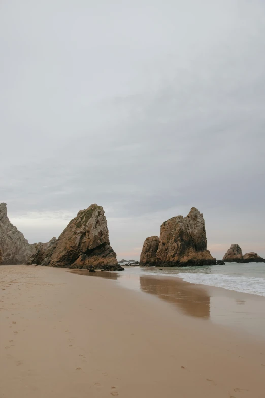 a sandy beach with two large rocks sticking out from the water