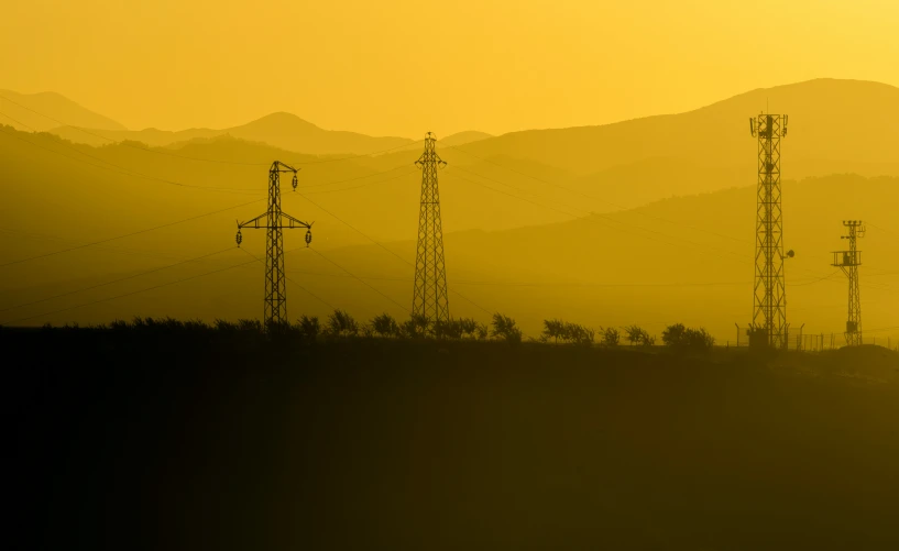 three silhouettes of electrical towers in front of a mountainous backdrop